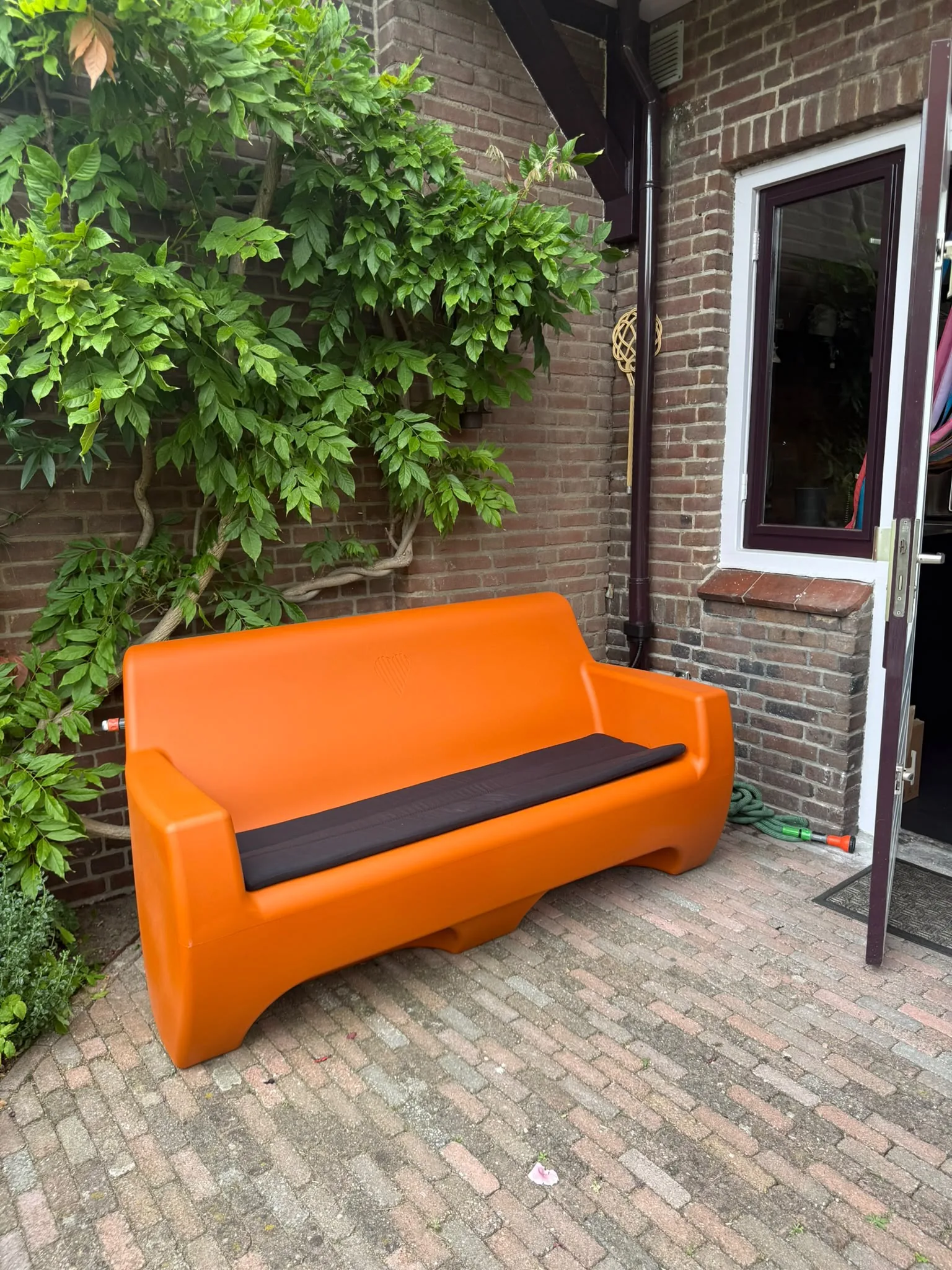 HappySofa regenbank in papaya oranje op een terras bij een bakstenen muur