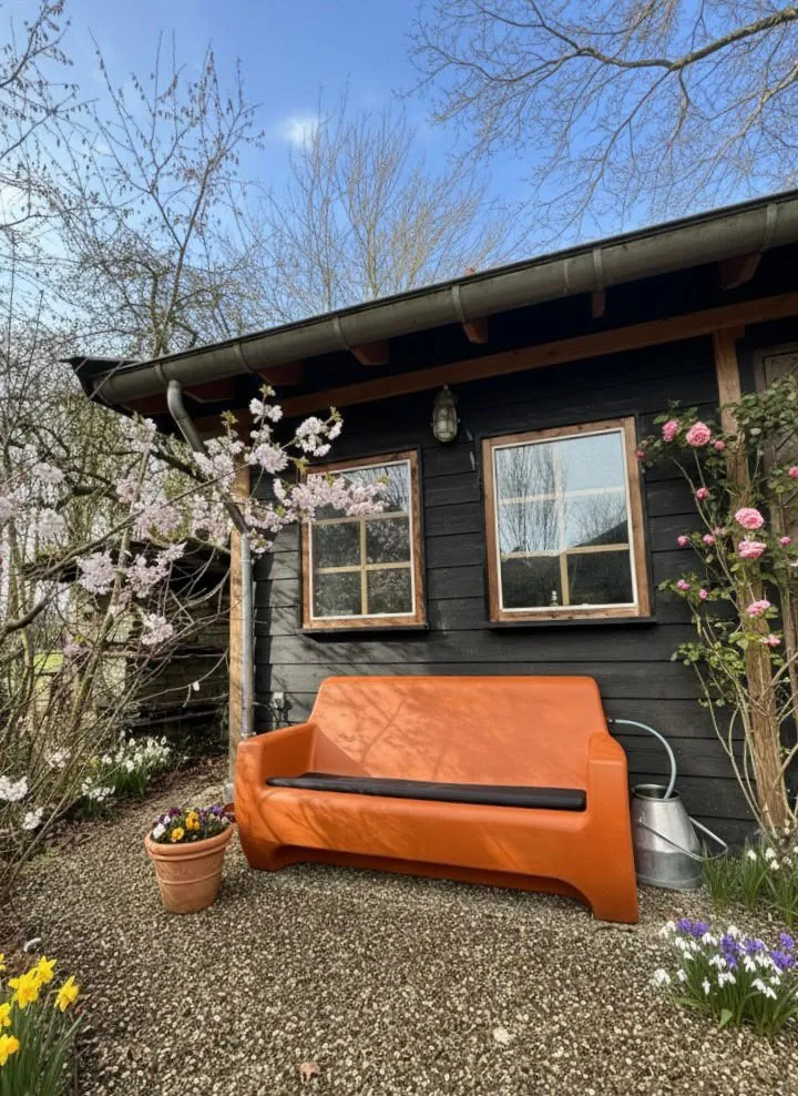 HappySofa regenbank in papaya oranje bij een tuinhuis met bloesem