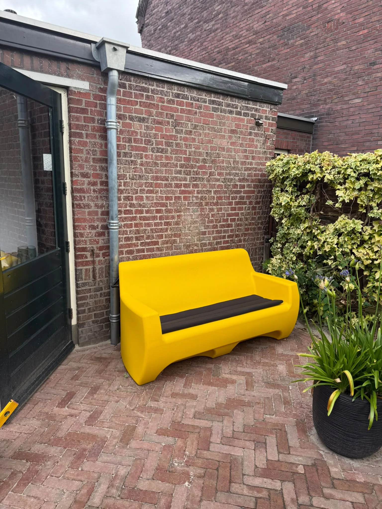 HappySofa regenbank in signaal geel op een terras naast de achterdeur