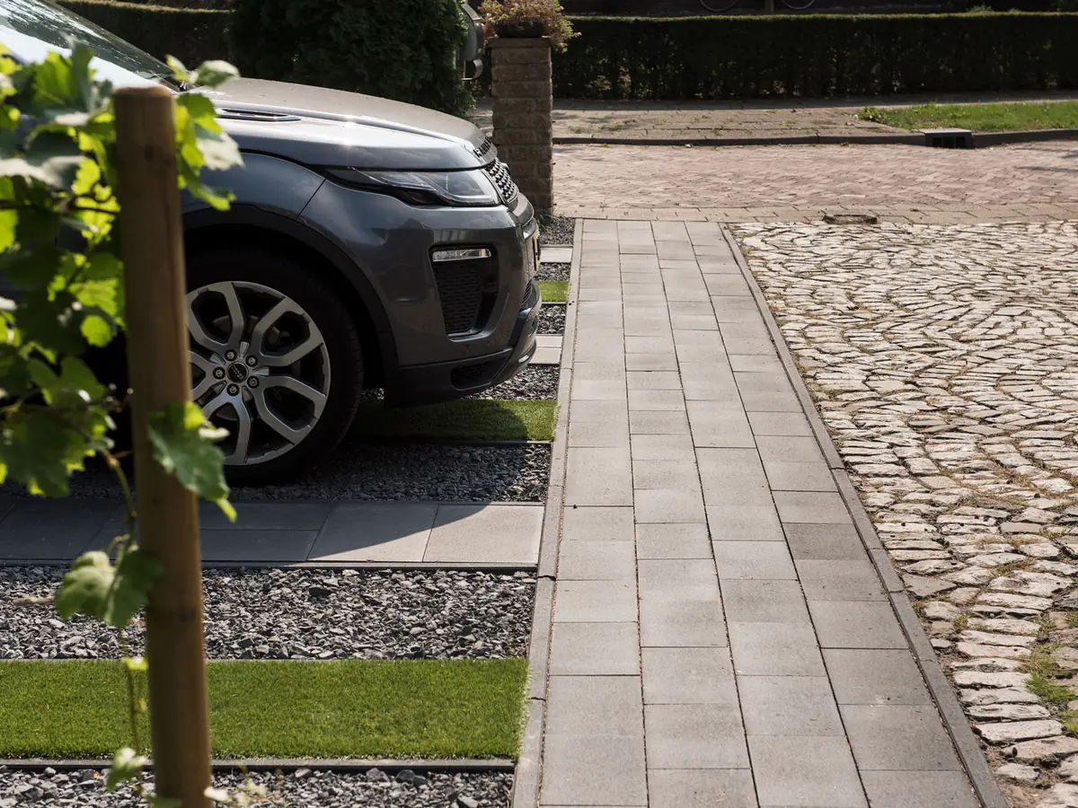 Oprit met een strook grind naast de bestrating, met geparkeerde auto