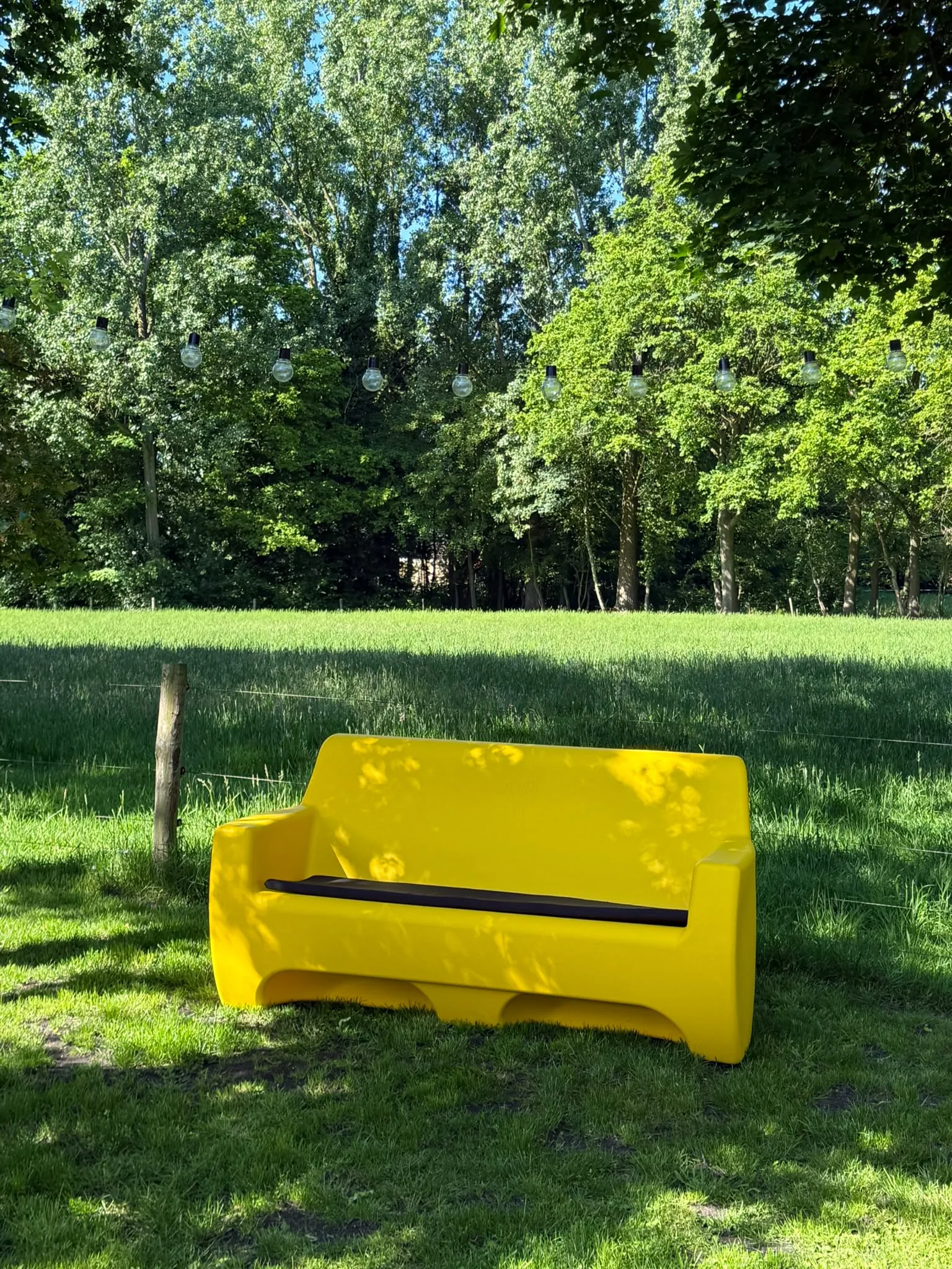 HappySofa regenbank in signaal geel in het gras onder de lichtjes