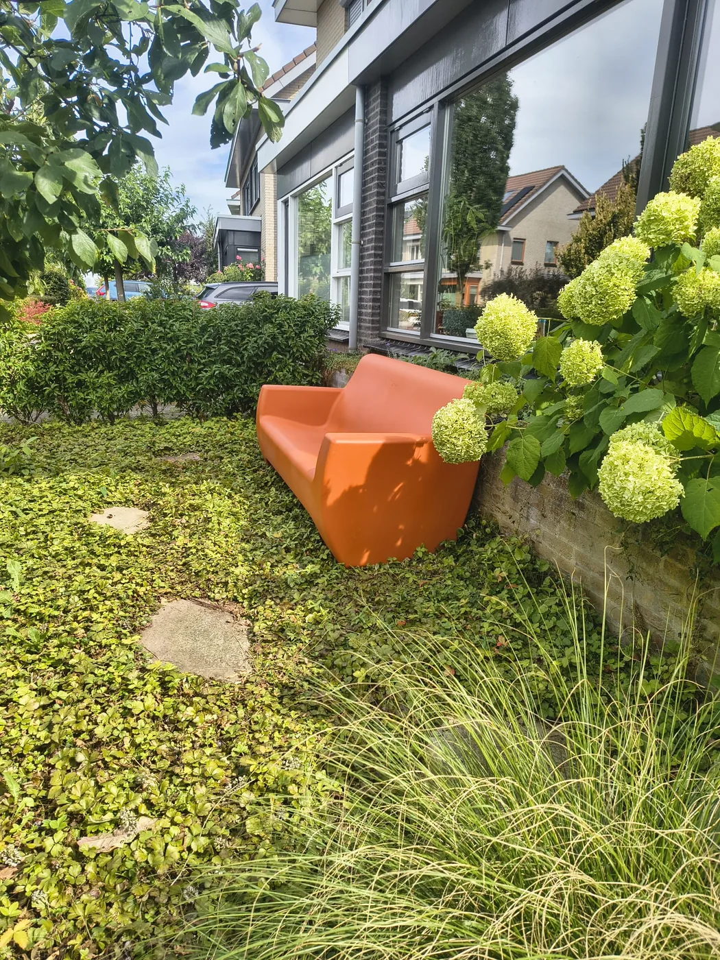 Papaya oranje HappySofa regenbank schuin van opzij, tussen hortensia's en siergras